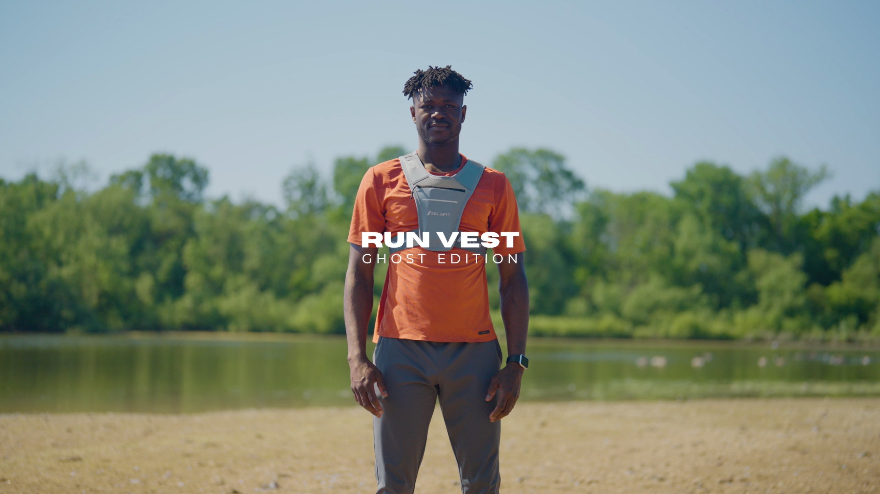 Male in front of lake shore wearing Run Vest Ghost Edition